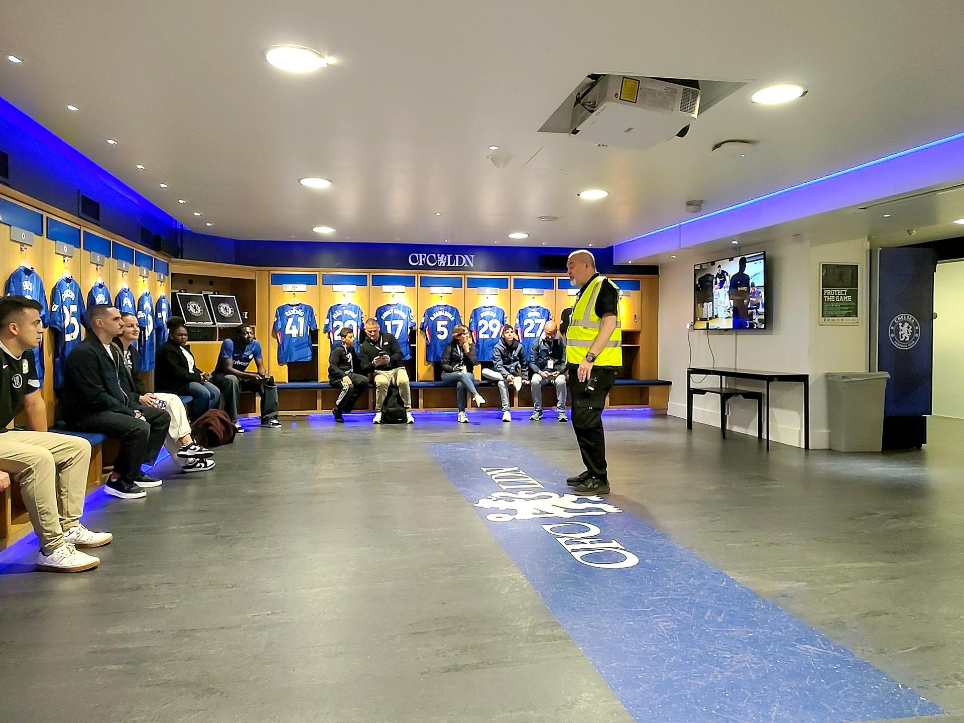 Przewodnik oprowadza grupę zwiedzających po szatni gospodarzy na Stamford Bridge