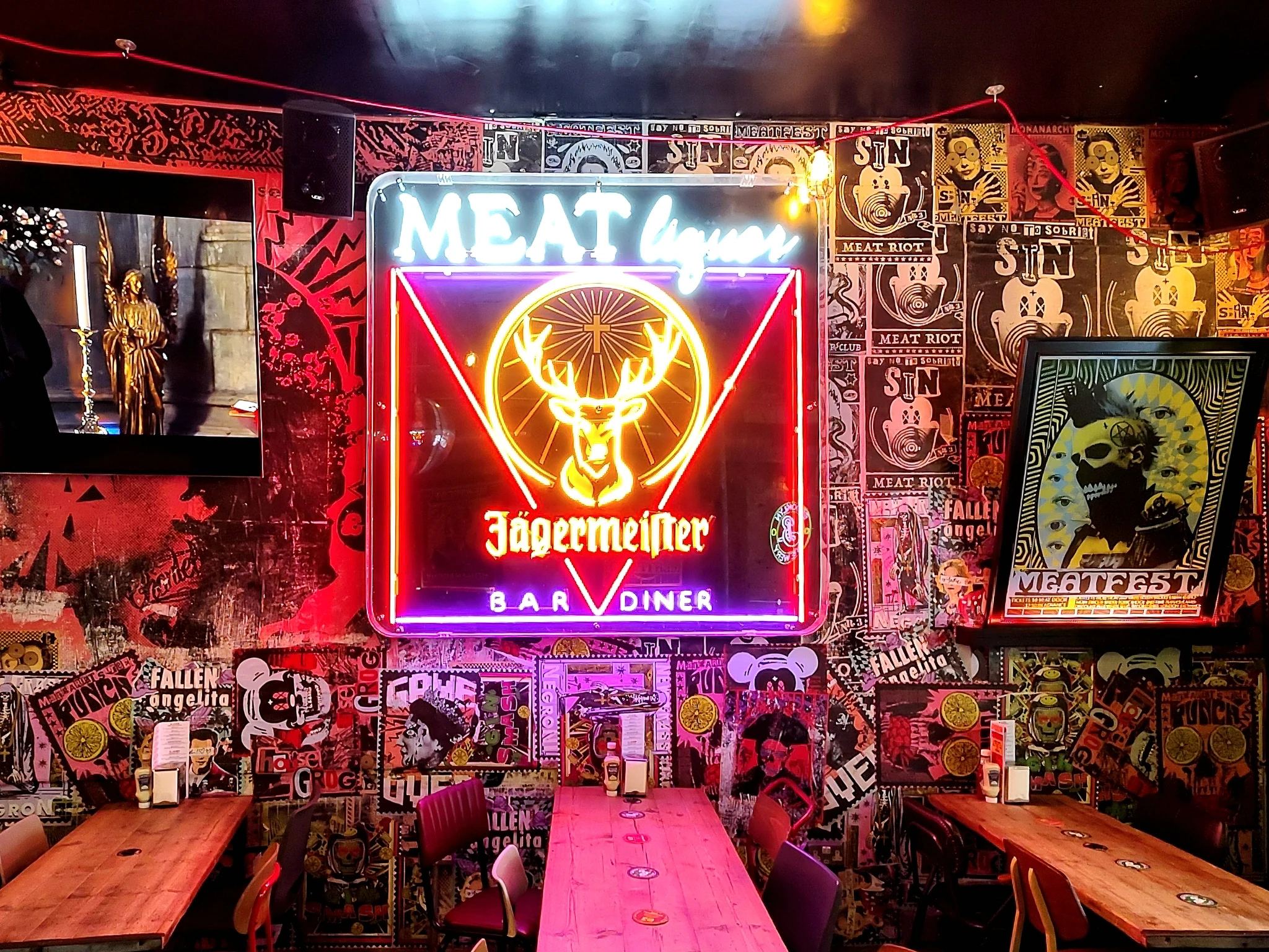 Neonowy szyld 'MEAT liquor' z logo Jägermeister nad barem w restauracji MEATliquor, ściana pokryta grafiti i plakatami