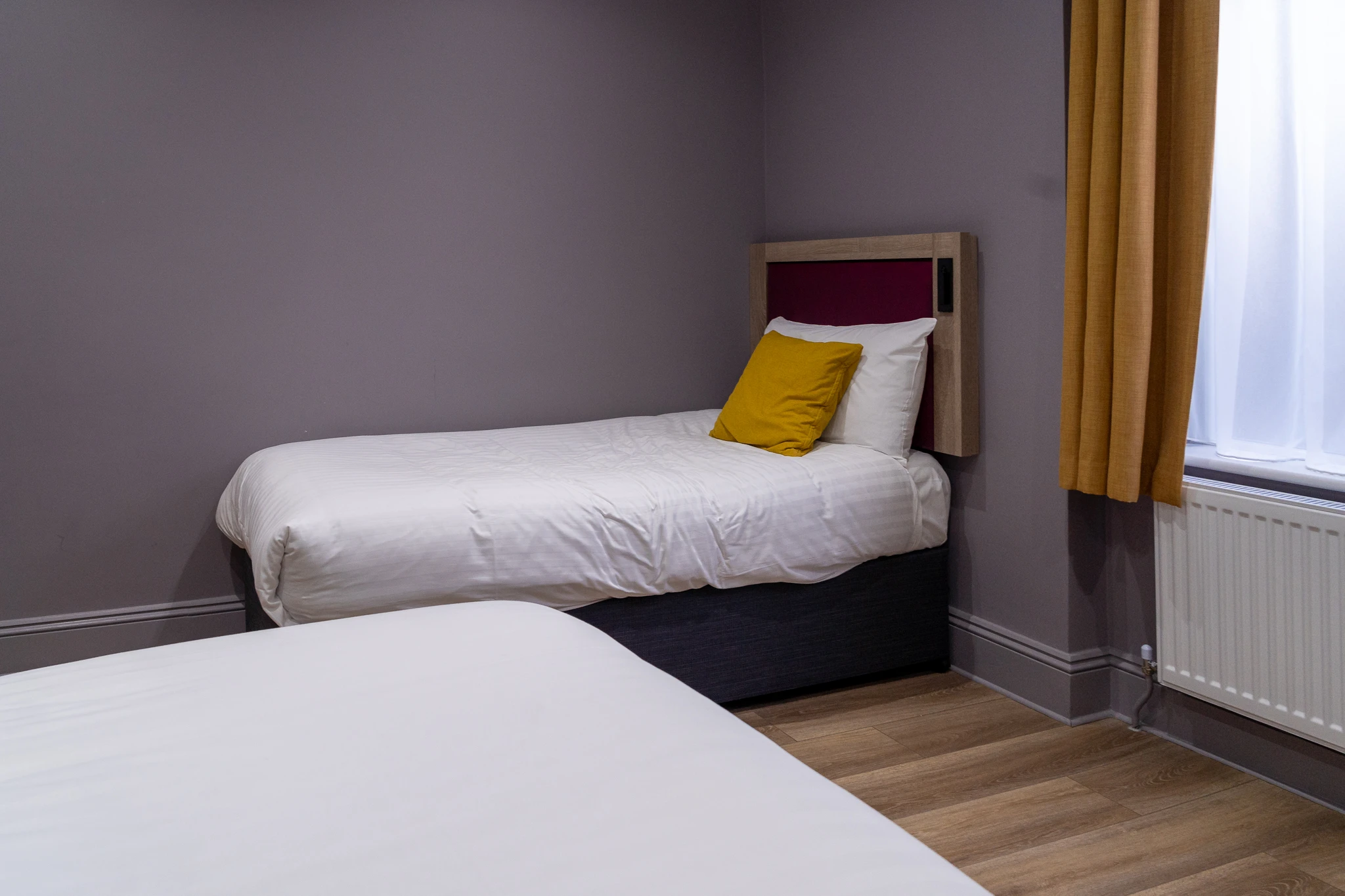 Pokój hotelowy Comfort Inn Edgware Road w Londynie, z dwoma pojedynczymi łóżkami, białą pościelą, żółtą poduszką i oknem z zasłonami.