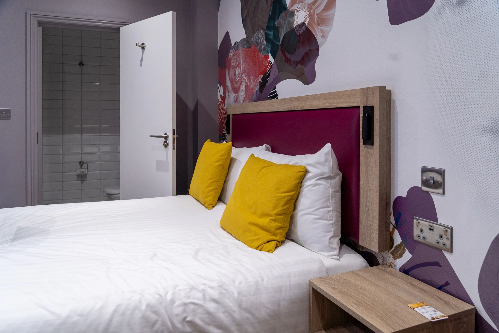 Jasny pokój hotelowy Comfort Inn London z wygodnym łóżkiem, żółtymi poduszkami i otwartą łazienką. Nowoczesny wystrój przy Edgware Road.