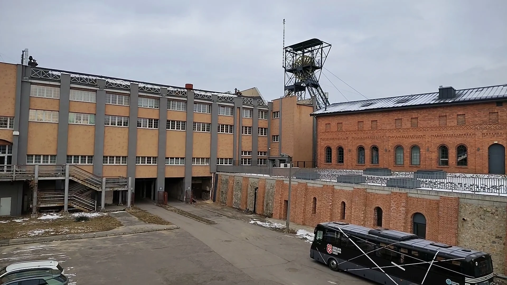 Widok na dziedziniec kompleksu kopalni Królowa Luiza w Zabrzu z budynkami, wieżą szybową i autokarem