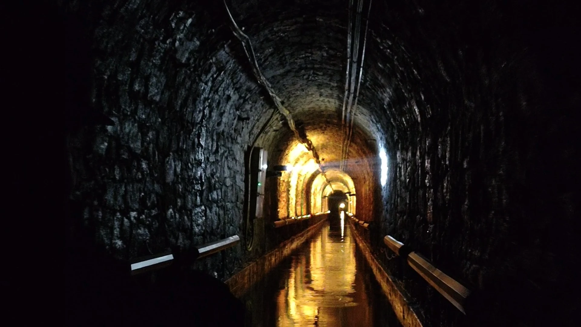 Zalany tunel z ciepłym oświetleniem odbitym w wodzie podczas podziemnego spływu w Sztolni Luiza w Zabrzu